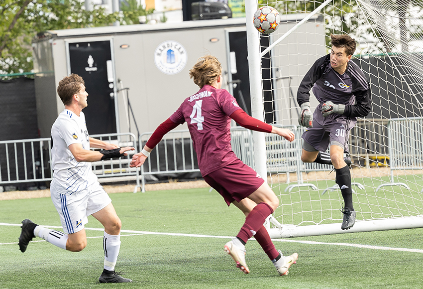 UNBCO keeper Ronan Woodroffe gets a hand on a ball in front of Jakob Sievert in the first half on Sunday (Rebecca Chelmick photo).