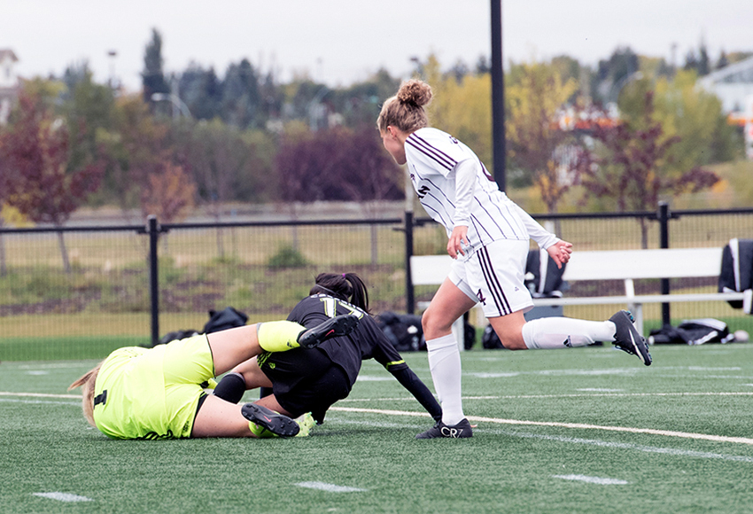 UFV's Gurneet Dhaliwal runs into diving MacEwan goalkeeper Emily Burns in the first half on Friday, while Samantha Gouveia looks on. There was no foul on the play, but Burns was assessed one for walking out of the box with the ball in her hands and it led to UFV's winning goal (Chris Piggott photo).